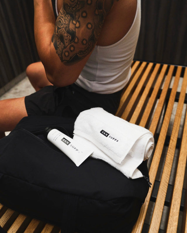 Man sitting on locker room bench post workout with SKN SUPPS Zinc Reset cleanser and towel on top of gym bag.