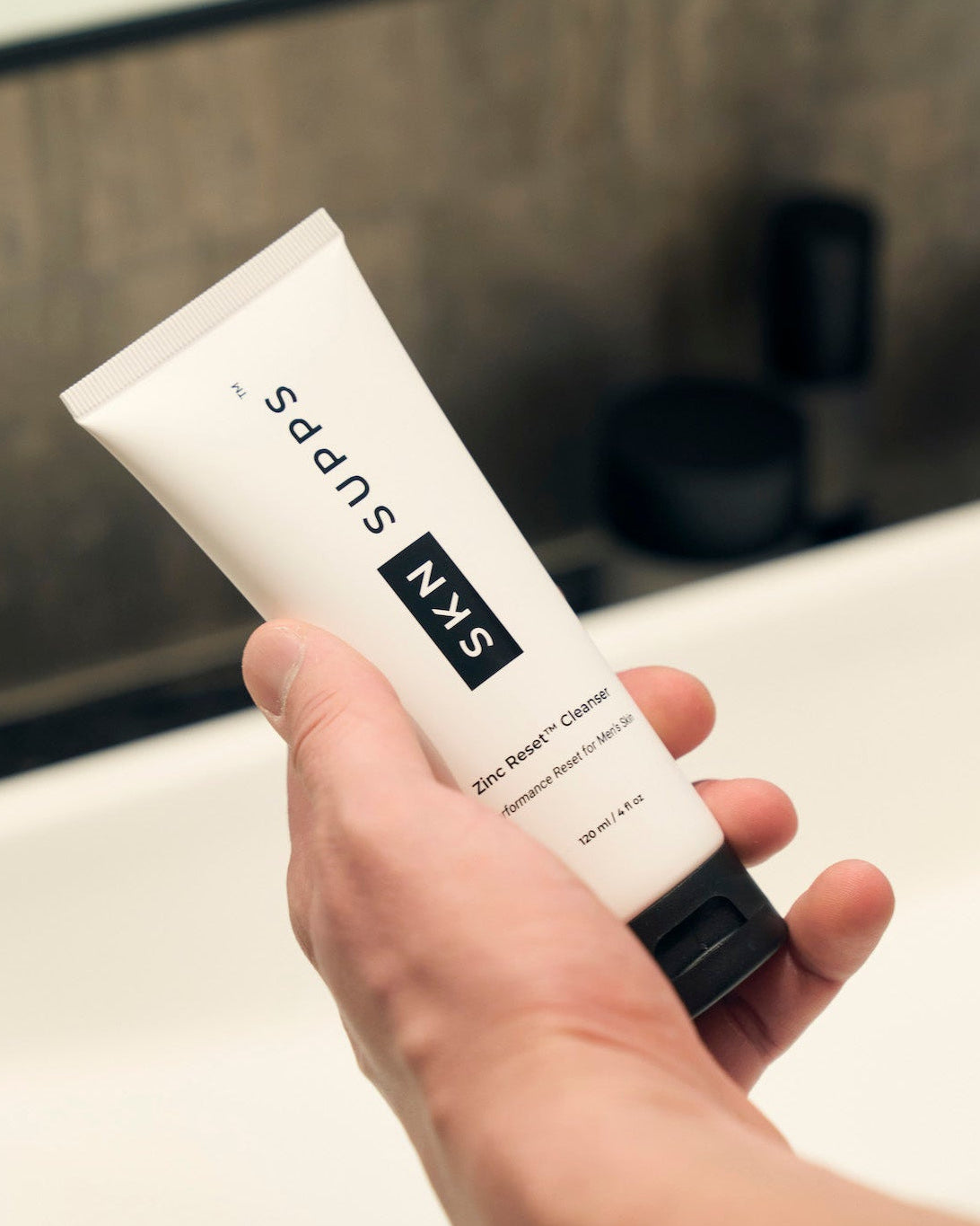 Man holding SKN SUPPS Zinc Reset daily face wash in bathroom.